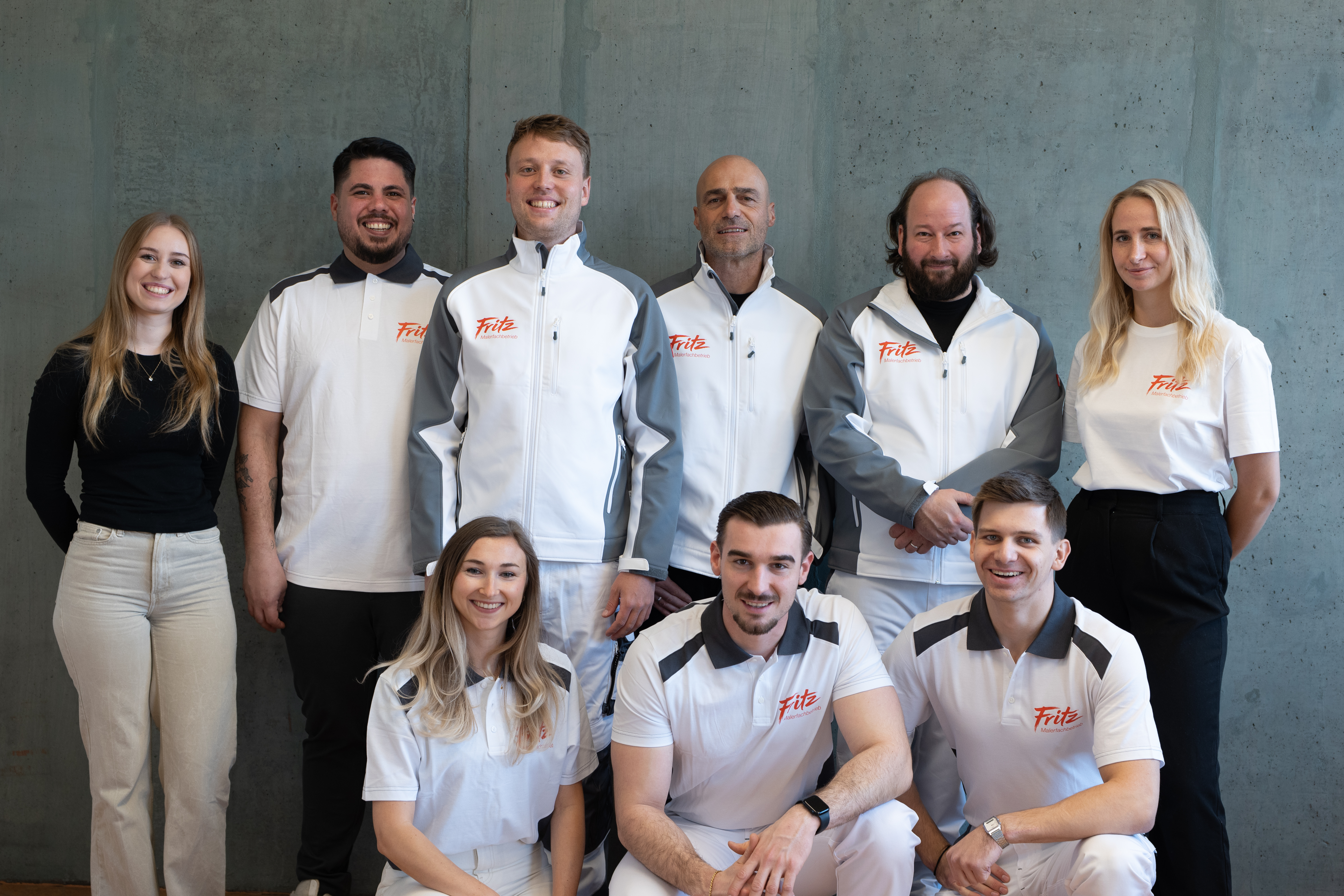 Nine smiling members of the Fritz painting company team pose together for a group photo