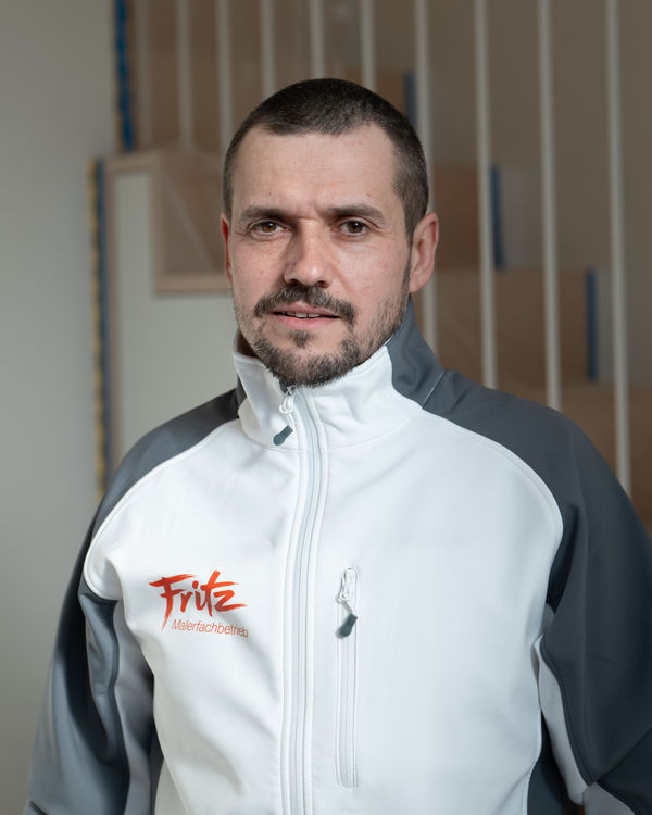 Henryk Knichalla, Head of Construction, wearing the Fritz painting company work jacket in front of an unfinished wooden staircase