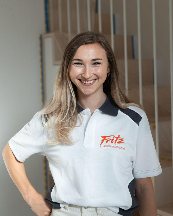 Leona, Planning and Interior Design, smiling in a Fritz painting company polo shirt in front of an unfinished wooden staircase