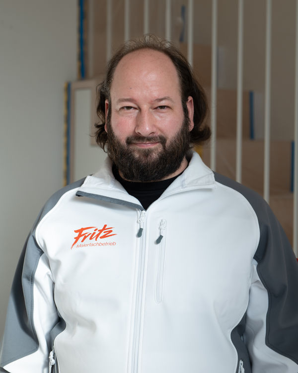 Volker, Team Leader and Painter, bearded and in a Fritz painting company work jacket in front of bright wall panels