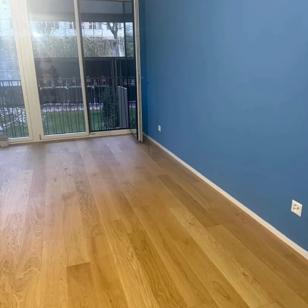 Innenanstrich einer Wohnung – Wohnraum mit blauer Akzentwand, weissen Wänden und Eichenparkett