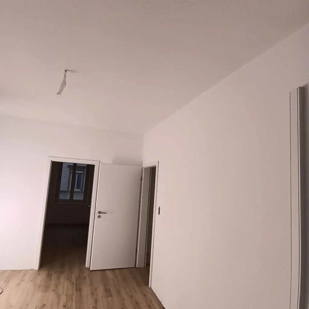Tapezierarbeiten in einer Wohnung – heller Korridor mit frisch tapezierten, weiss gestrichenen Raufaser-Wänden und Laminatboden